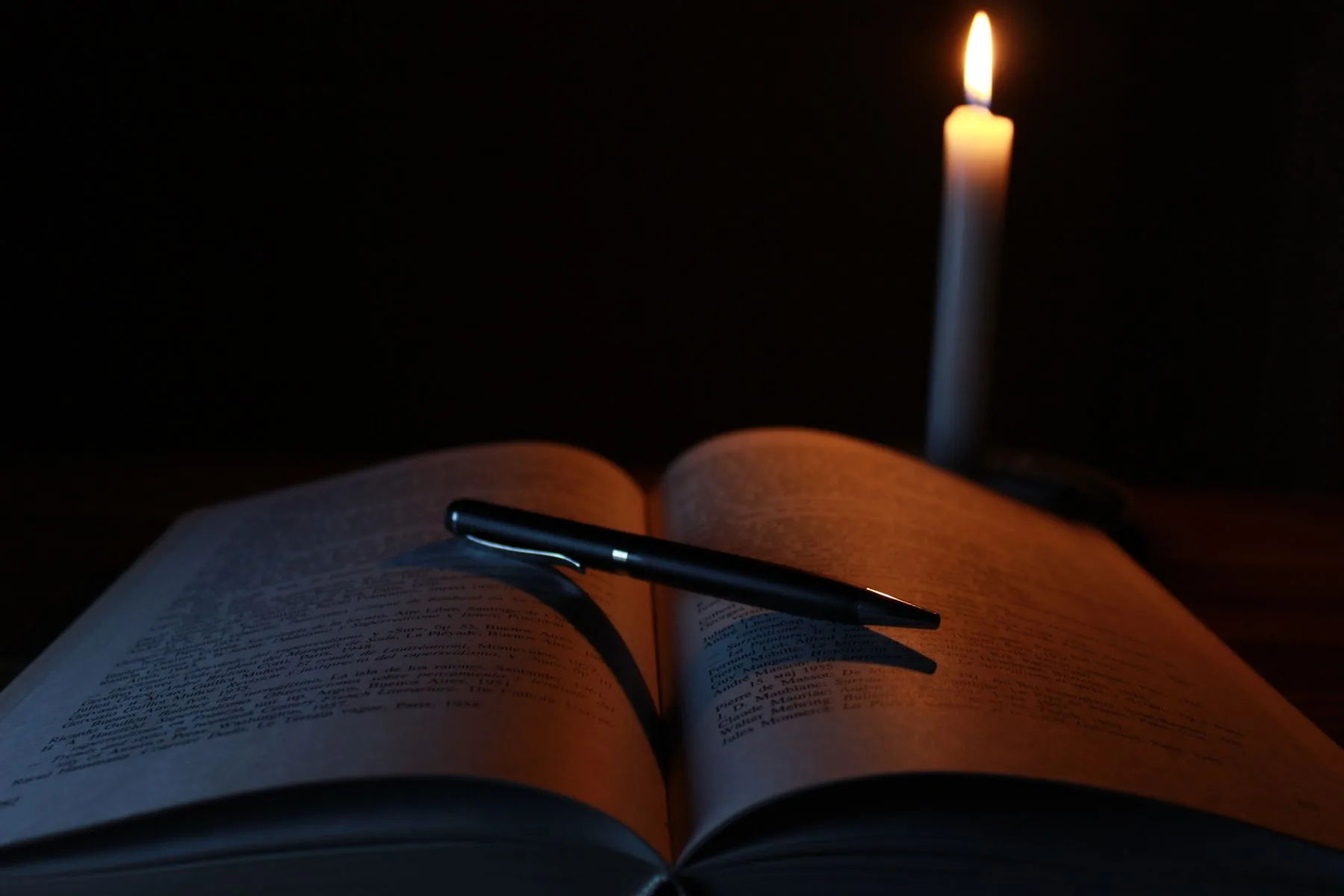 An open book beside a single lit candle at night