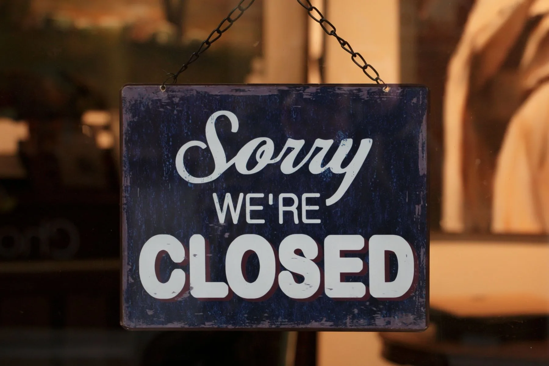 A vintage Sorry We're Closed sign hanging in a shop window, warmly lit