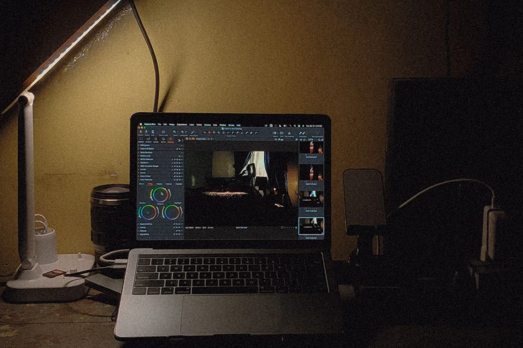 A laptop left glowing alone on a desk in a dark room, lit only by a desk lamp
