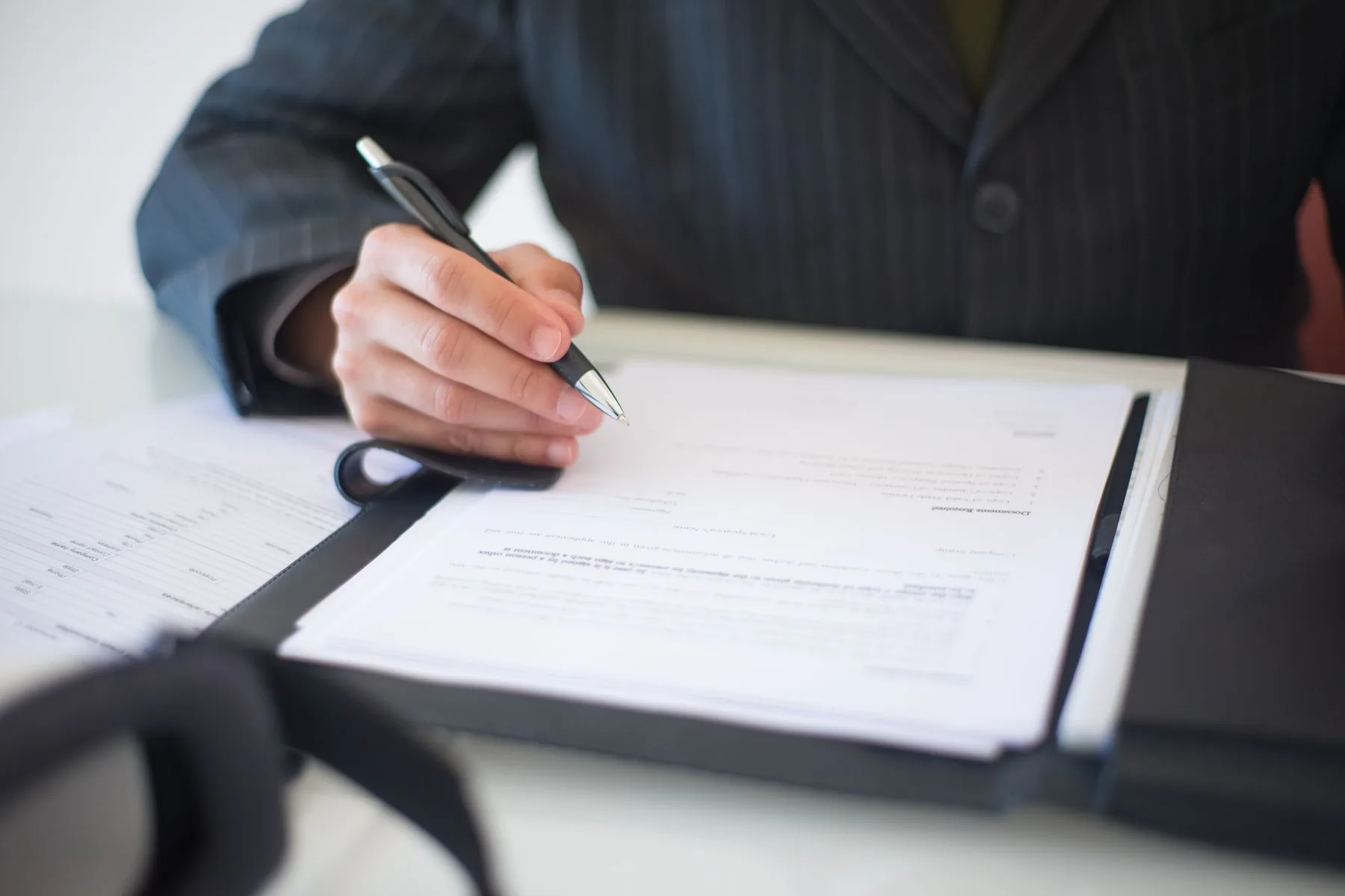 A person in a suit signing a document on a clipboard