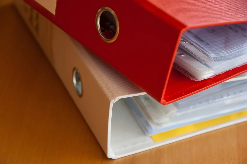 Two ring binders, one red and one tan, stacked and stuffed with papers and tabs
