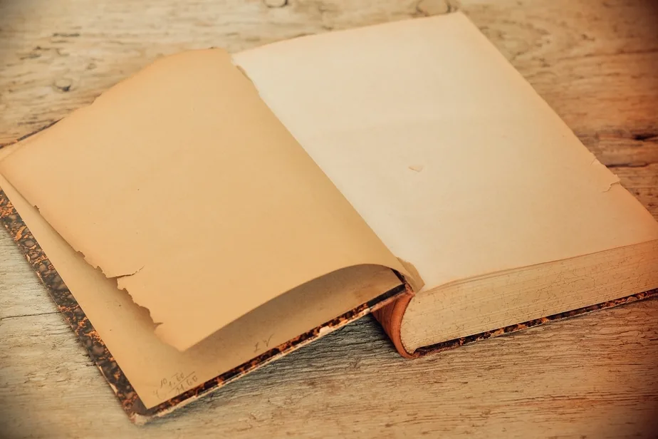 An old open book with blank, sun-faded pages resting on a worn wooden table