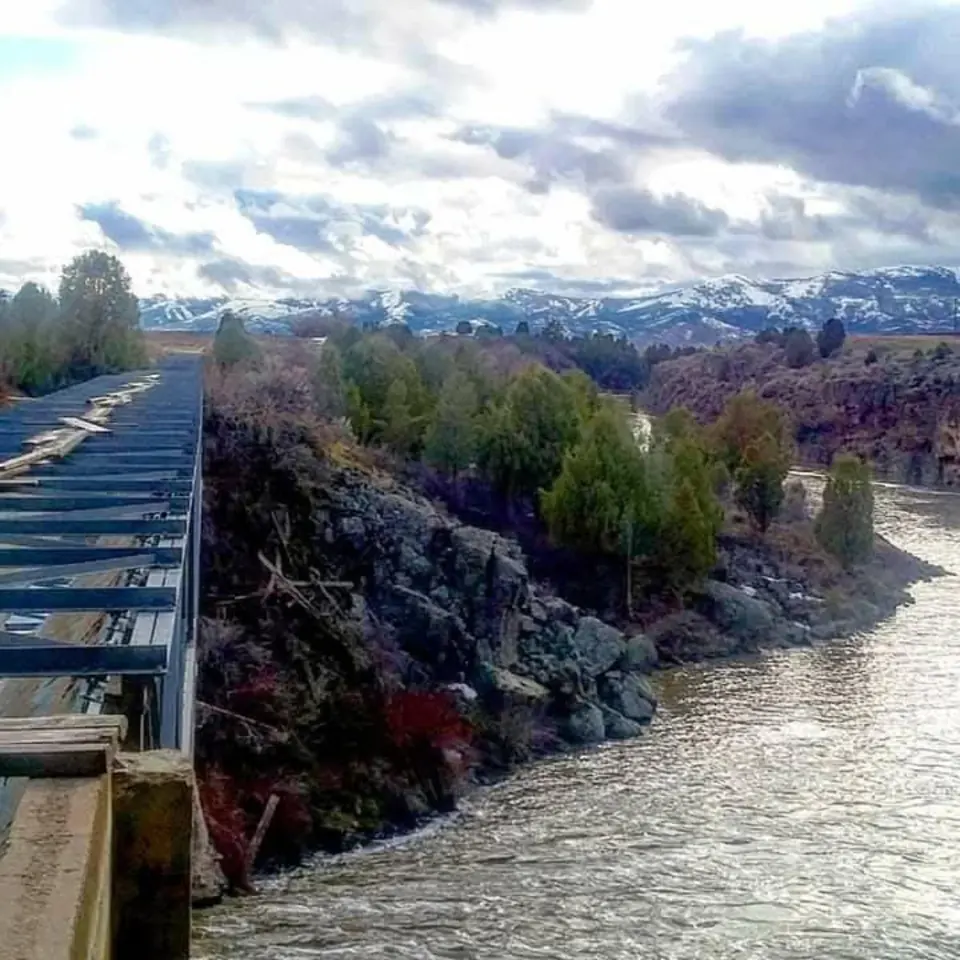 An aging wooden bridge above a rocky river canyon with mountains in the distance, photographed by Craig Rothchild