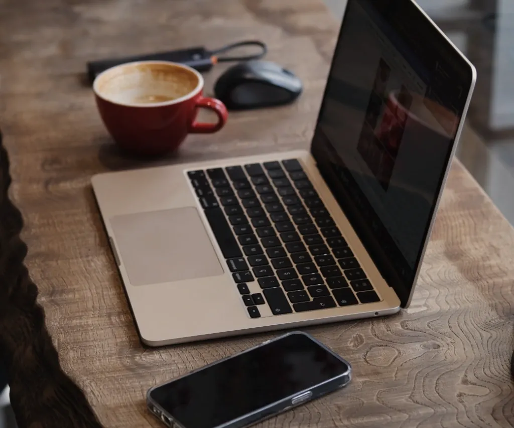 A laptop, phone and cup of coffee on a wooden table, ready to get the details down